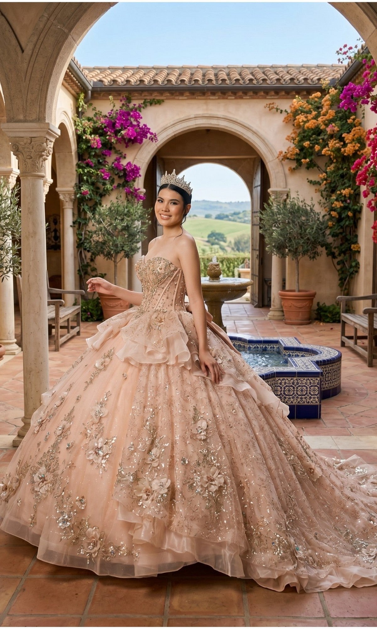 A young woman stands in a courtyard with arches, blooming flowers, and a tiled fountain, wearing the Quinceanera Dress 8590JQ by Cinderella Couture—an elaborate pink ball gown with a glitter tulle skirt and beaded corset bodice.